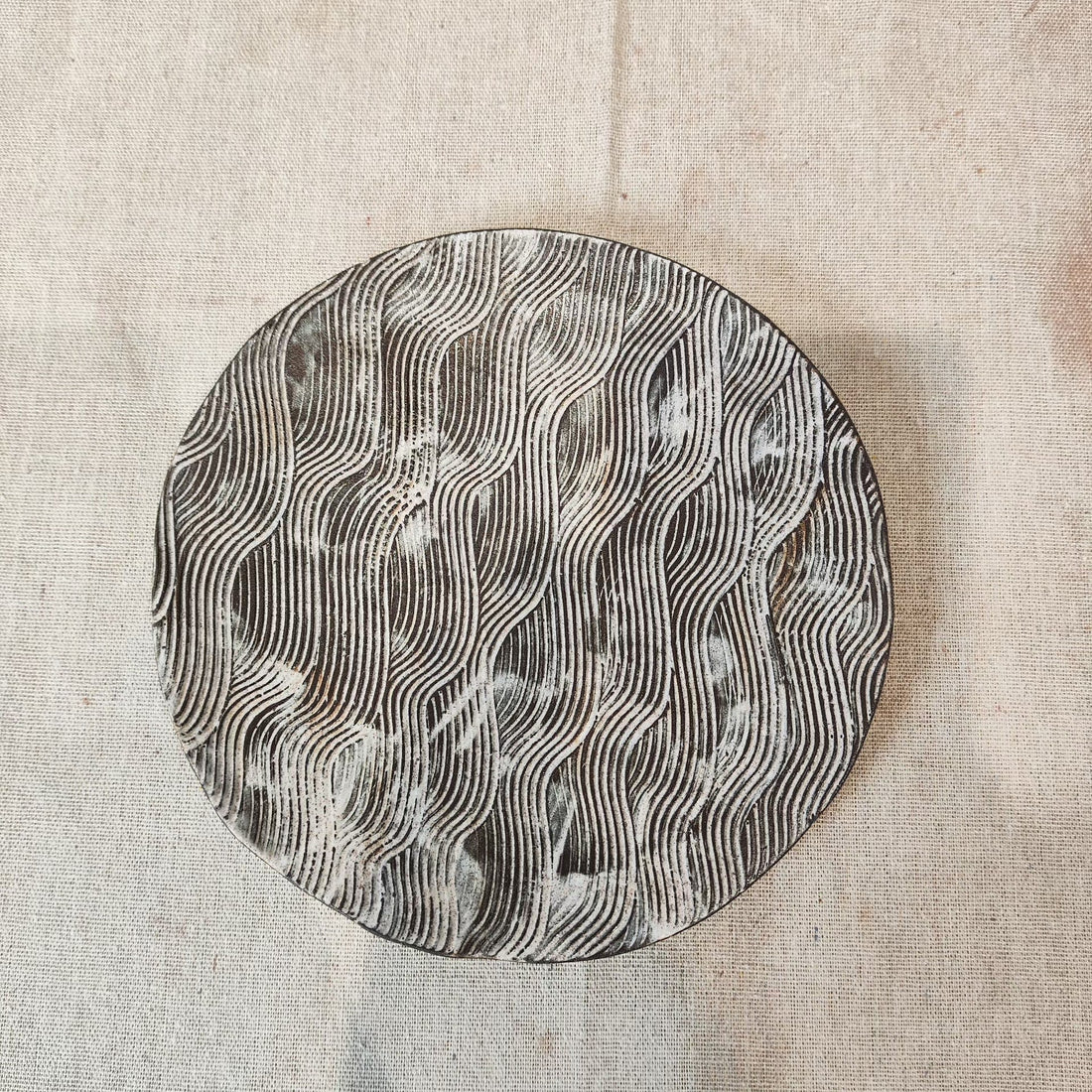 Round black ceramic plate with pale carved wave lines
