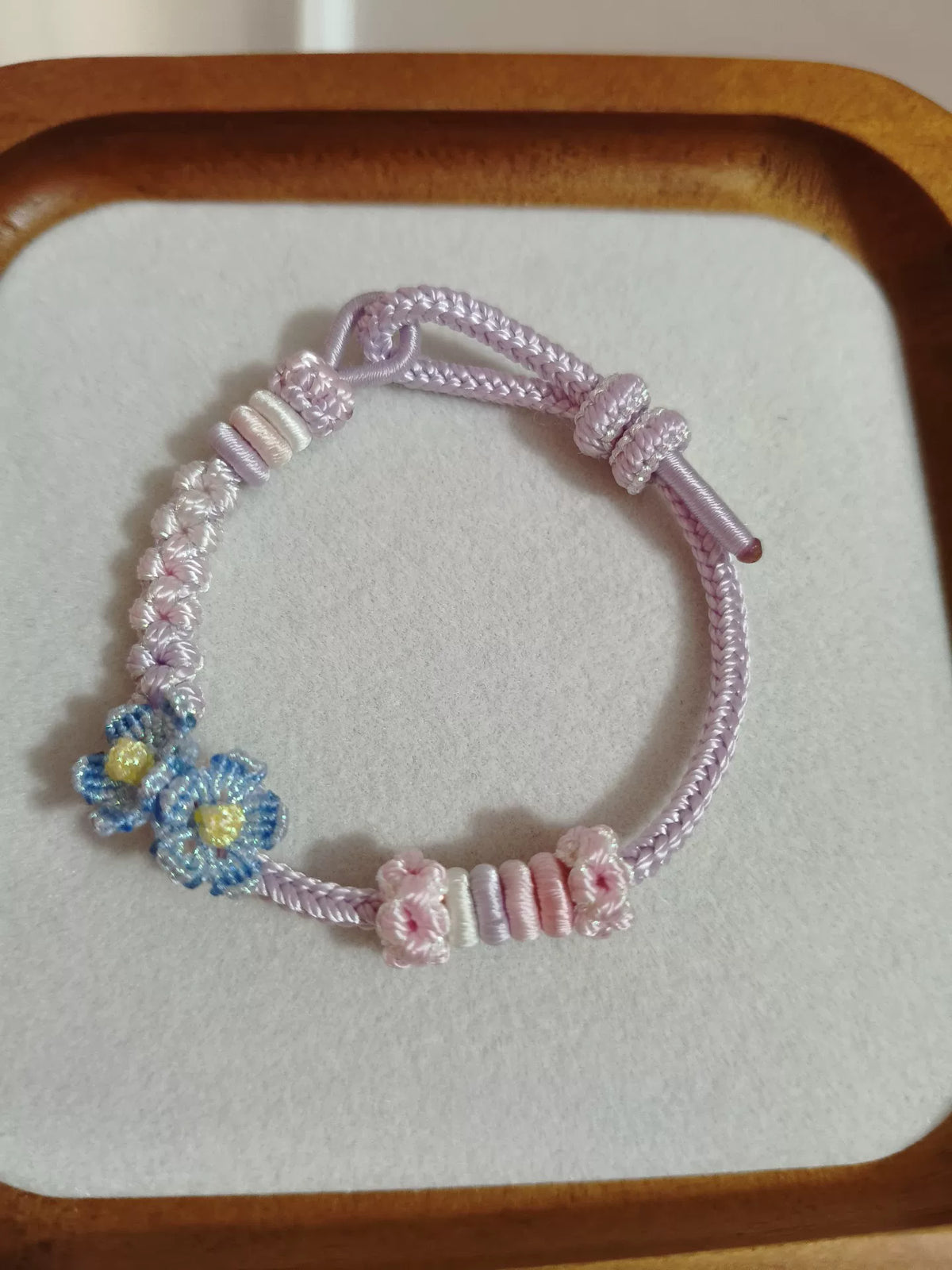Handgjort flätat armband i rosa gradient med blå blommor